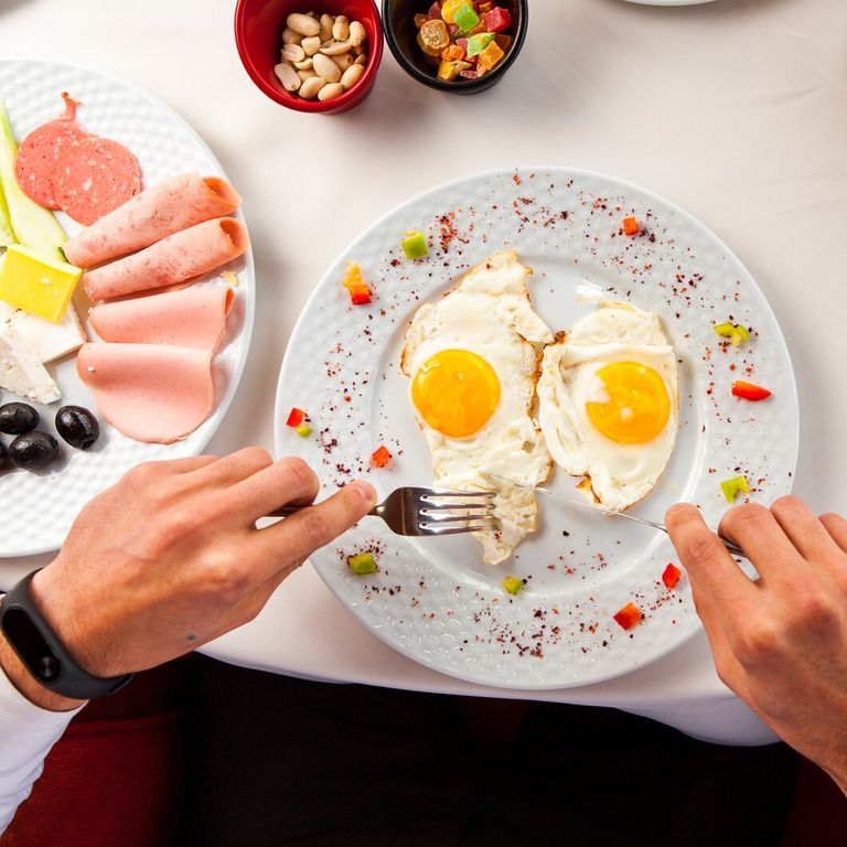 top-view-fried-eggs-table-white-tablecloth-plate-with-olives-cheese-ham-with-nuts-candied-fruits-hands-man-with-fork-knife-breakfast_176474-922.jpg