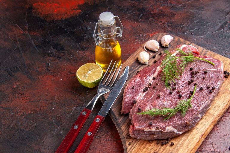 top-view-red-meat-wooden-cutting-board-garlic-green-pepper-oi-bottle-fork-knife-dark-background_140725-141359.jpg