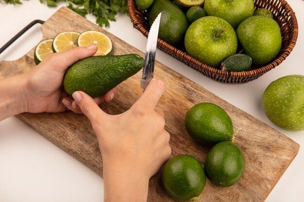 top-view-female-hands-cutting-fresh-avocado-with-knife-wooden-kitchen-board-with-limes-with-apples-bucket-white-wall_141793-76038.jpg