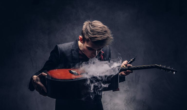 handsome-young-musician-with-stylish-hair-in-elegant-clothes-exhales-smoke-on-his-acoustic-guitar-isolated-on-dark-background.jpg