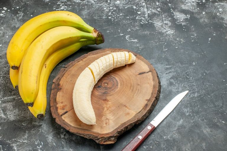 front-view-nutrition-source-fresh-bananas-bundle-chopped-wooden-cutting-board-knife-gray-background_140725-140116.jpg