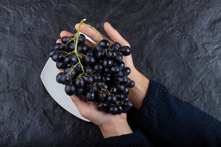 male-hands-holding-bunch-black-grapes-black-background_114579-42345.jpg