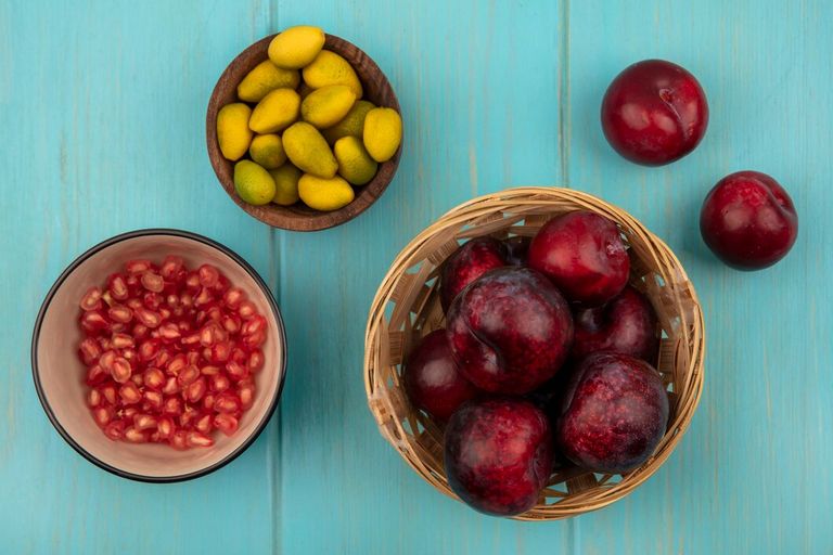 top-view-fresh-pluots-bucket-with-pomegranate-seeds-bowl-with-kinkans-wooden-bowl-blue-wooden-background_141793-84575.jpg