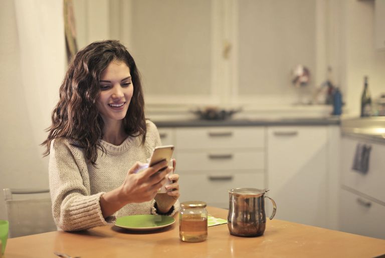 young woman drinking tea and using smartphone to chat online