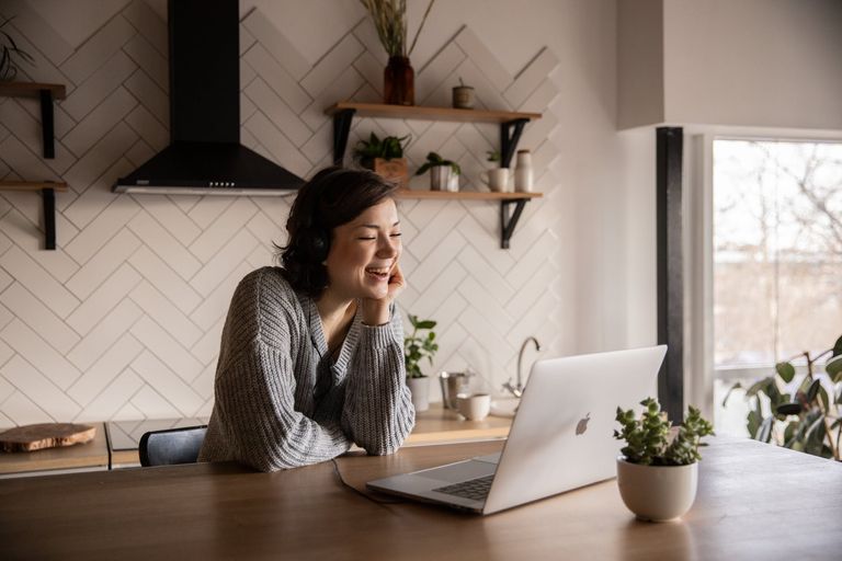 smiling woman having a video call via laptop in kitchen over websites to chat 